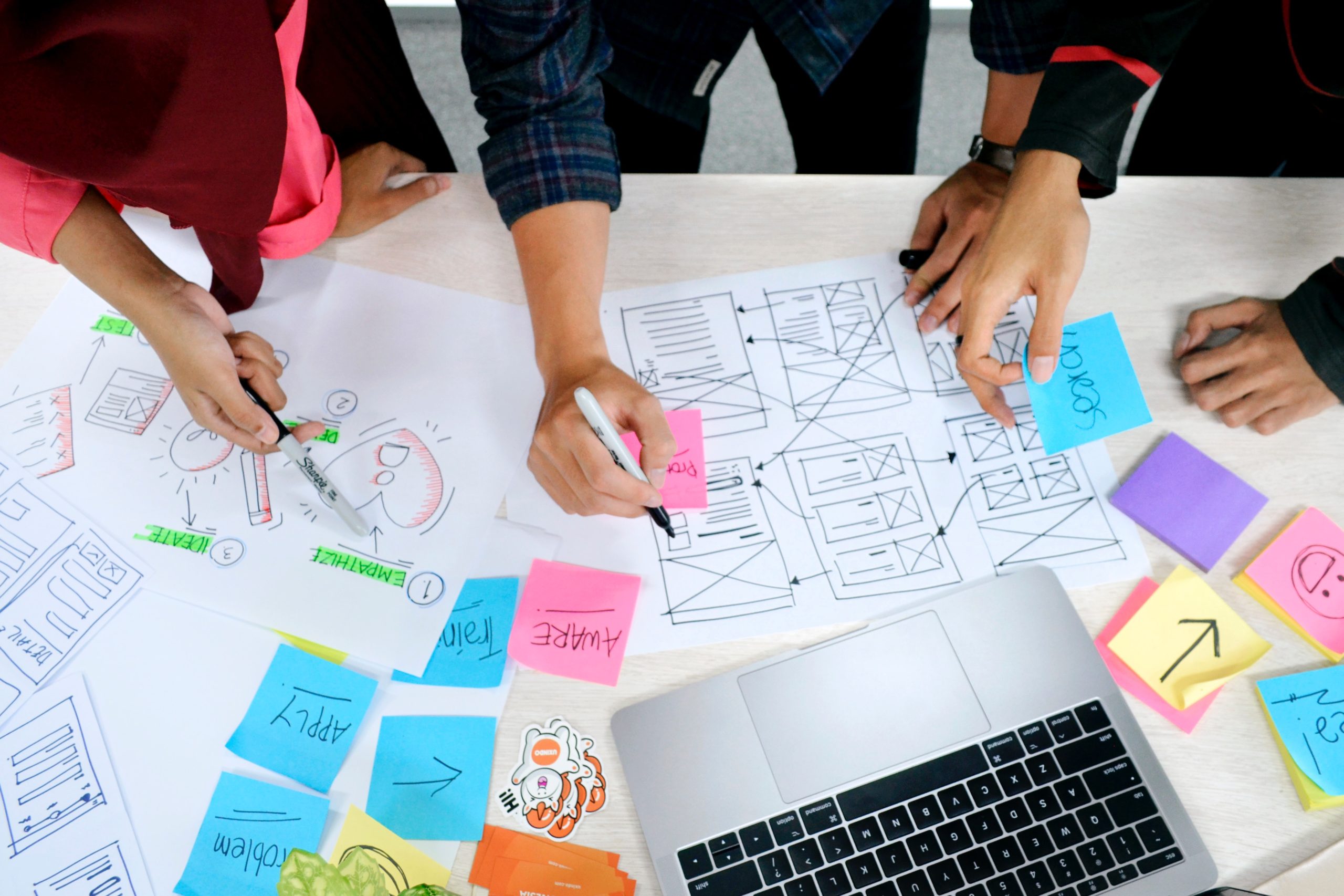 Three people working on a Design Thinking project with sticky notes and paper on a table