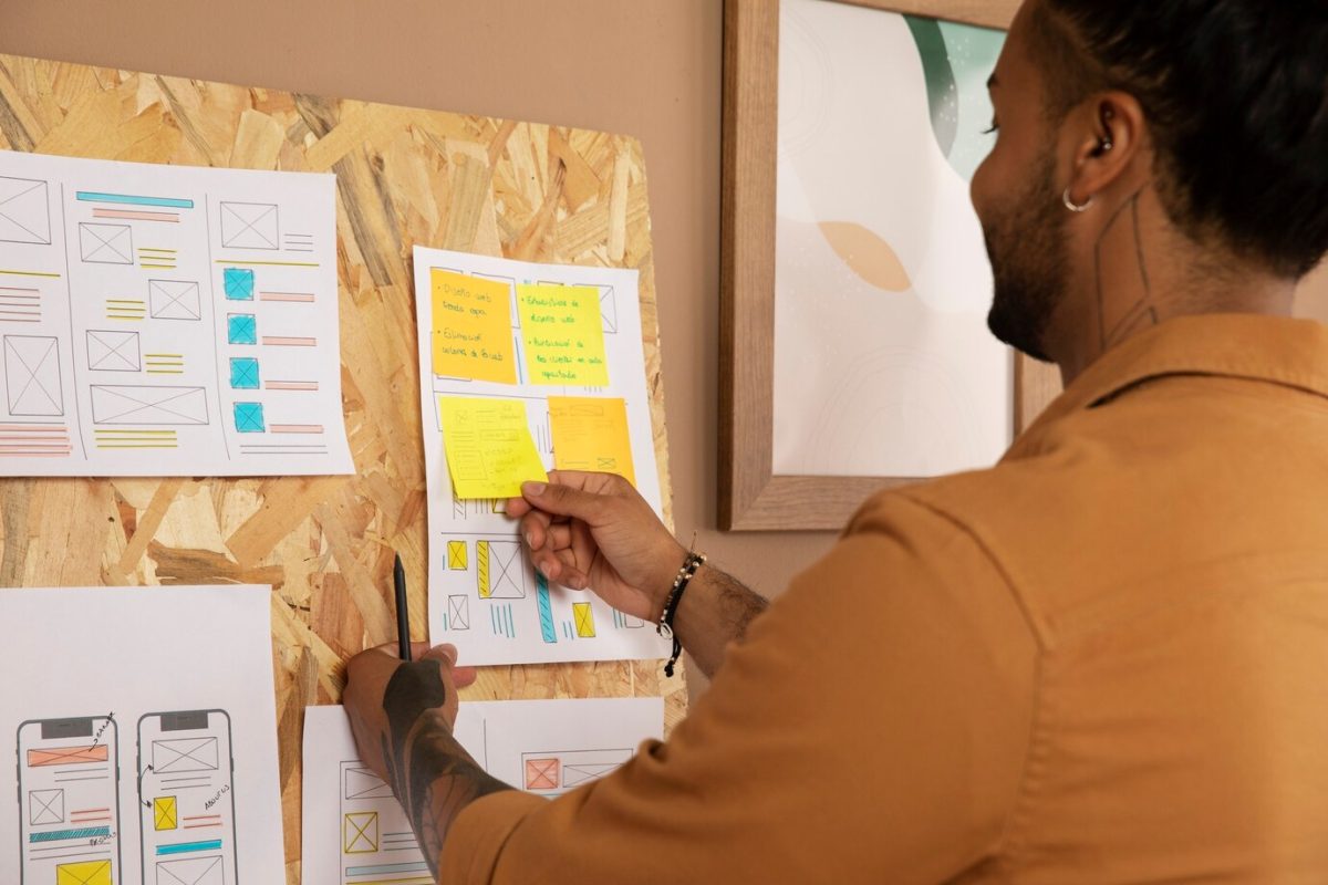 A designer puts up sticky notes on a planning board for a usability project. Credit: Freepik