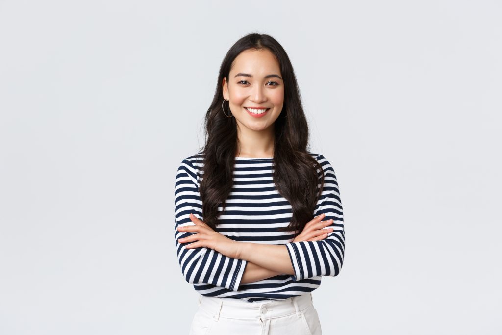 A woman with long black hair and a striped shirt with her arms crossed.