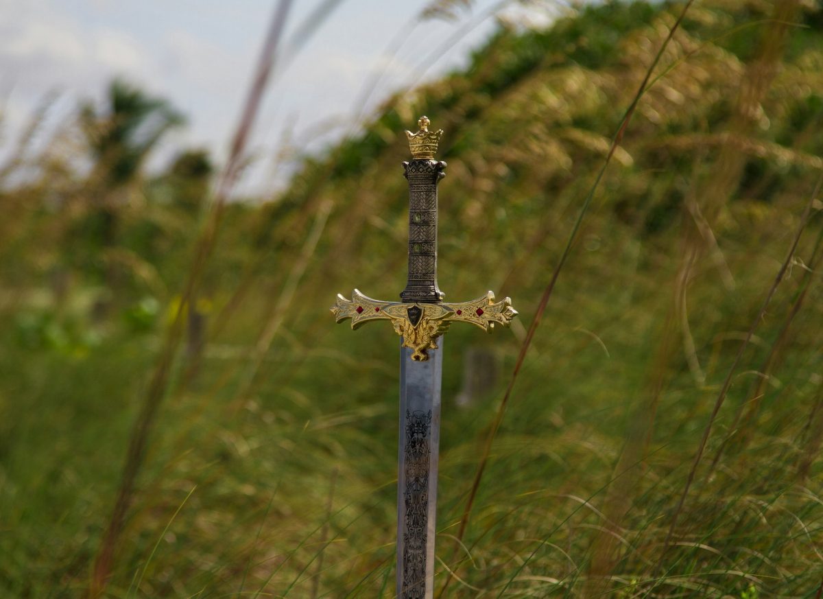 A sword with a golden hilt stands in a field. Image credit: Ricardo Cruz Unsplash.